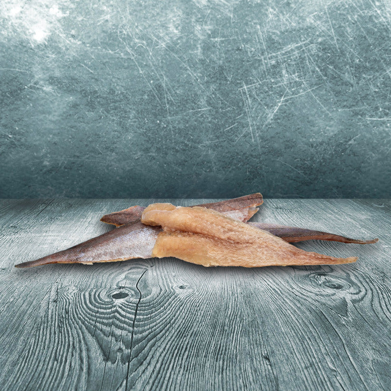 Gefrorene Stücke Seehechtfilet auf grauer Holzoberfläche vor blau-grauem Hintergrund