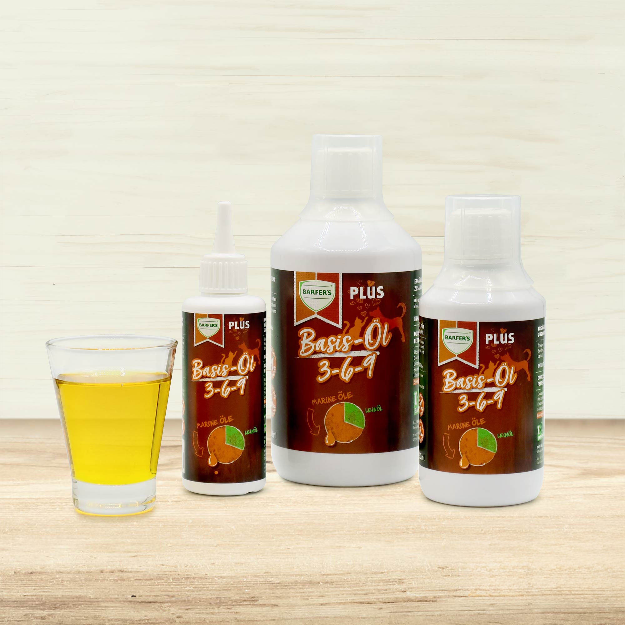 Drei unterschiedlich große weiße Flaschen BARFER’S Basis-Öl 3-6-9 mit braun-orangefarbenem Etikett und Glas mit gelbem Öl, auf hellem Holzuntergrund vor heller Holzwand