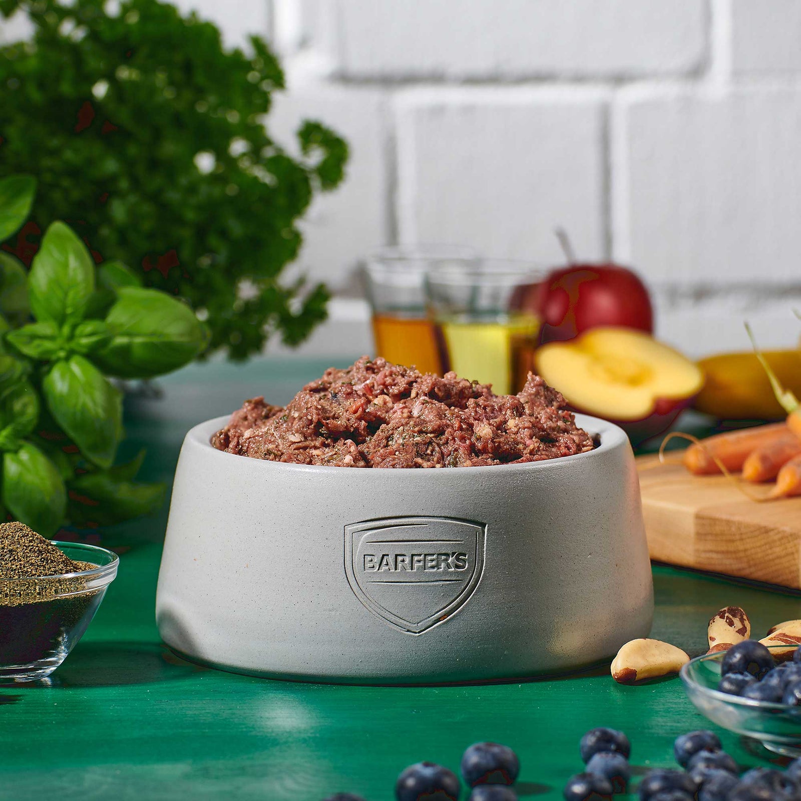 BARFER’S Napf gefüllt mit Komplett-Mix Pferd für Hunde – im Hintergrund frisches Obst, Gemüse, Öl und Seealgenmehl als Zutaten für vollwertiges Fertigbarf mit DLG-Zertifizierung