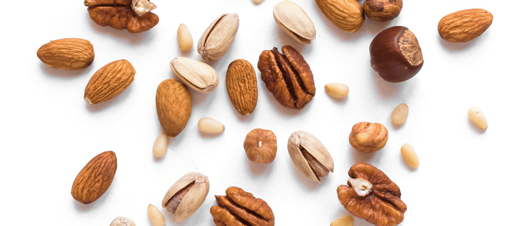 Verschiedene Nüsse und Kerne – Mandeln, Pistazien, Pekannüsse, Pinienkerne und Haselnüsse auf weißem Hintergrund