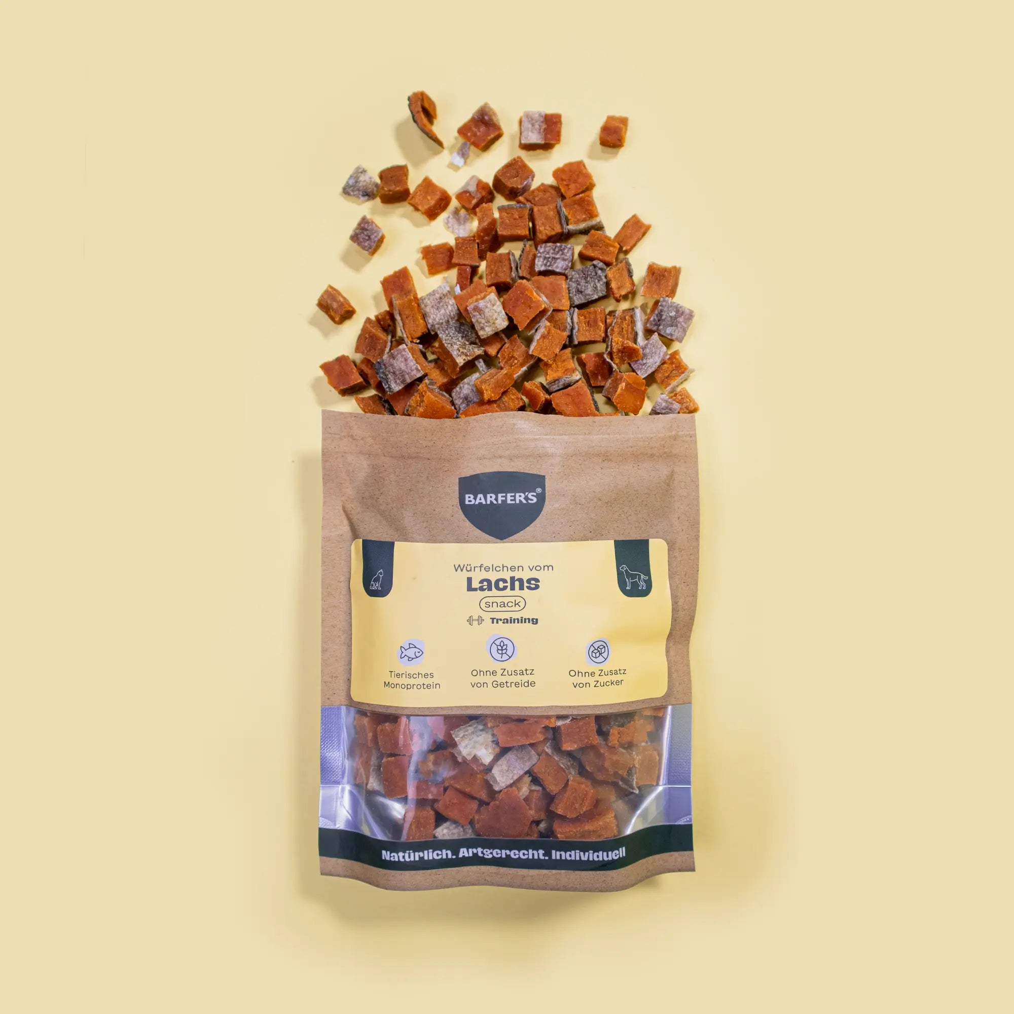 Gewürfelte und luftgetrocknete Leckerli vom Lachs liegen oberhalb einer geöffneten Verpackung "Würfelchen vom Lachs" der Marke BARFER’S