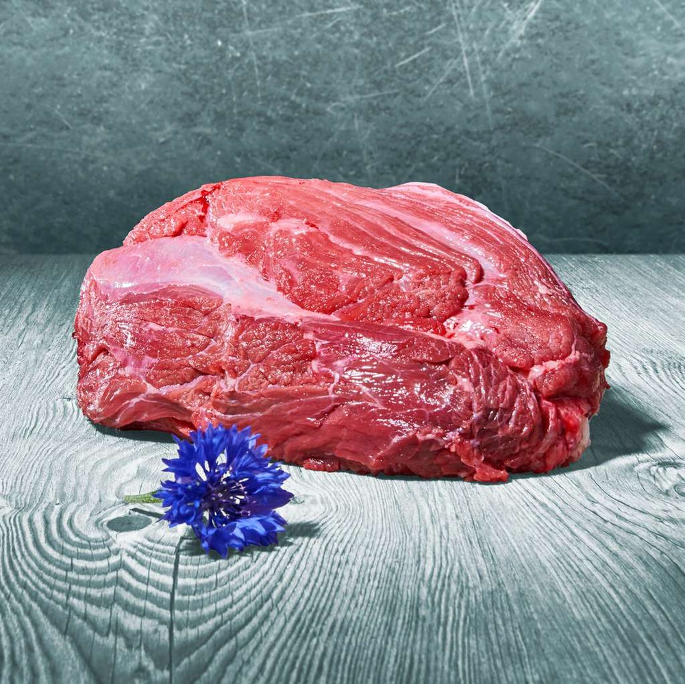 Großes Stück rohes Rindfleisch auf Holztisch mit blauer Blume dekoriert