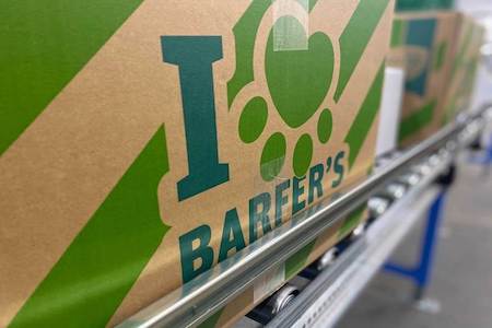 Grüne BARFER’S Versandverpackung für Frostware mit großem „I love BARFER’S“-Logo auf einem Förderband in der Lagerhalle