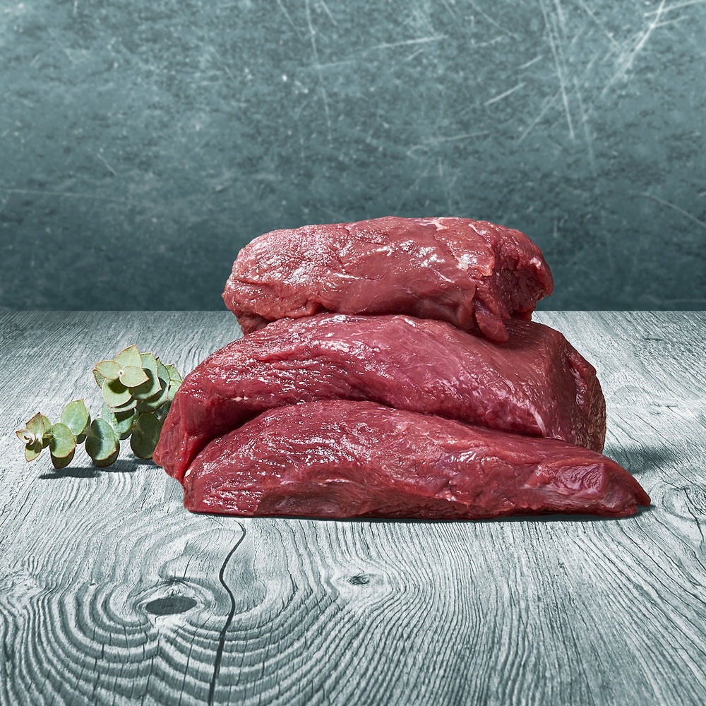 Rohe Stücke vom Kängurumuskelfleisch auf einer Holzoberfläche mit grünem Zweig als Dekoration