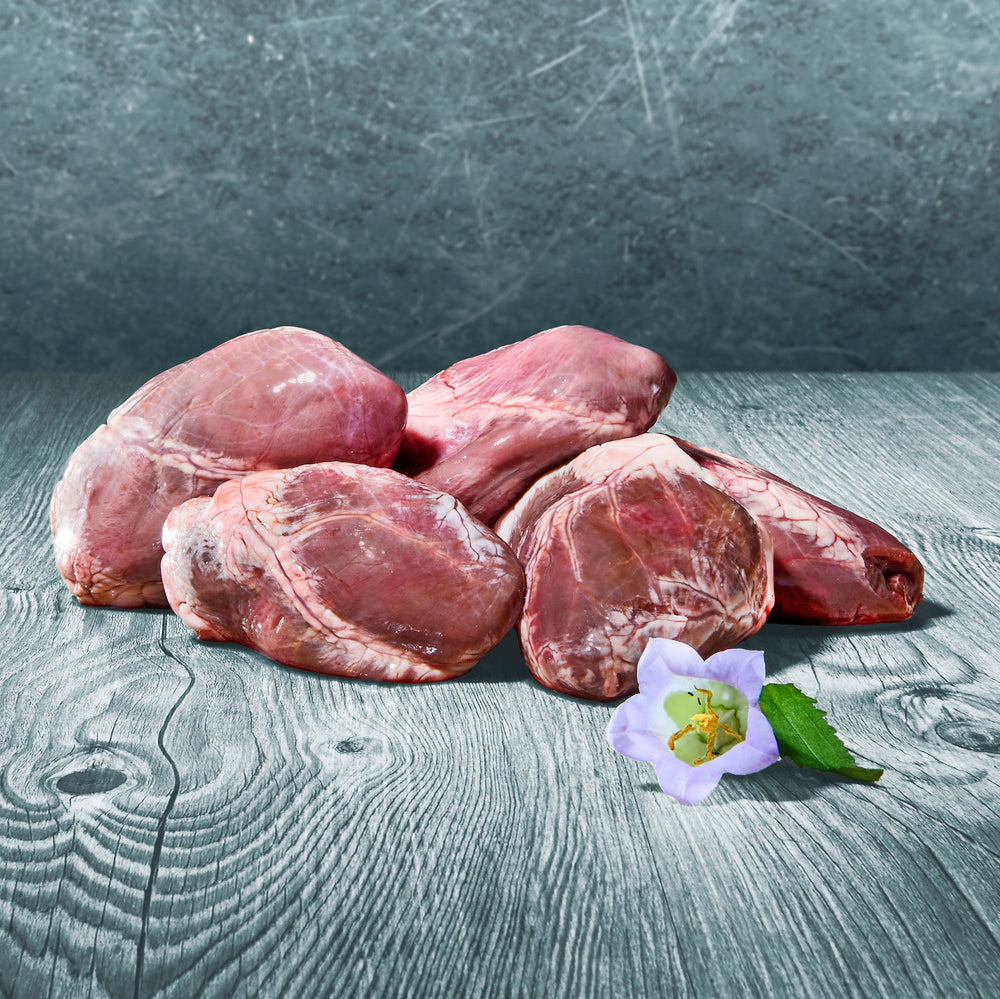 Ganze BARF-Lammherzen auf einer Holzoberfläche, dekoriert mit einer violetten Blüte