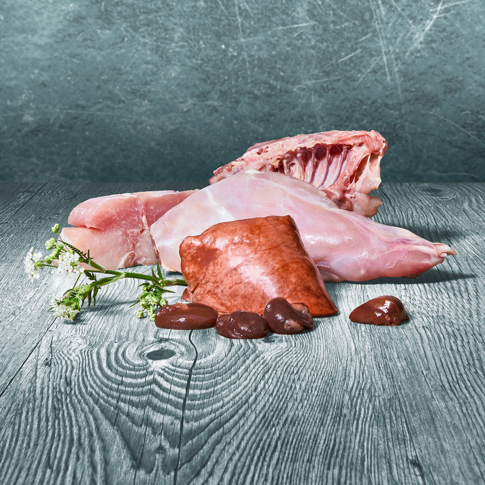 BARFER’S Pur-Mix Kaninchen Zutaten im Überblick – Kaninchenfleisch, Kaninchenkarkasse, Kaninchenherz, Kaninchenleber, Kaninchenlunge und Kaninchenspeiseröhre, roh und frisch präsentiert mit weißen Blüten auf grauer Holzoberfläche