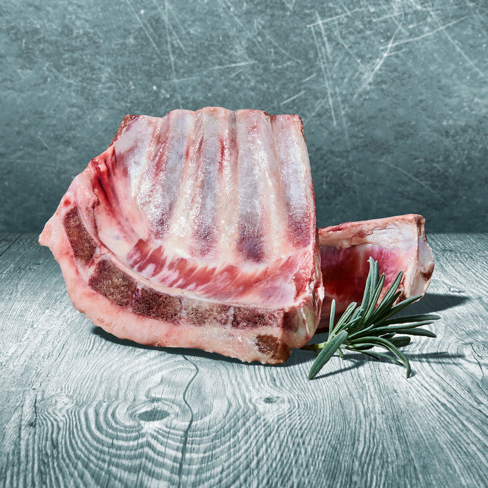Rohes Stück Lammrippen auf Holztisch mit Rosmarinzweig dekoriert