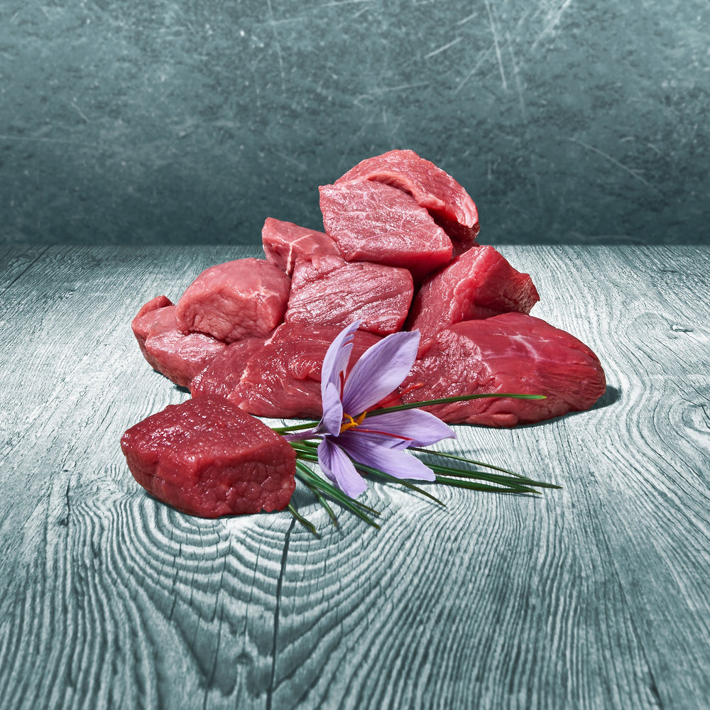 Rohe Stücke mageres BARF-Rindfleisch auf Holztisch mit violetter Blüte dekoriert