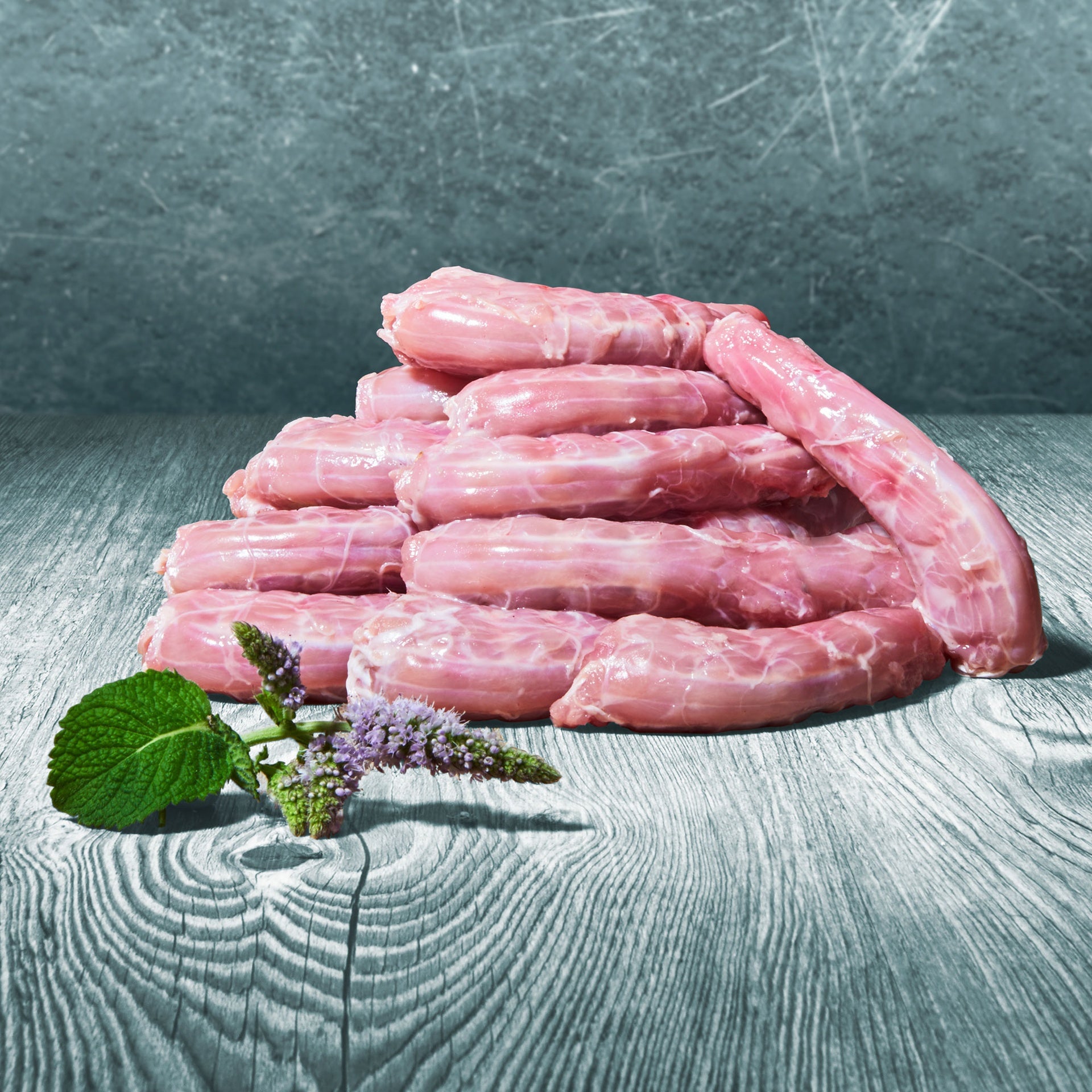 Rohe BARF-Hühnerhälse auf grauer Holzfläche, dekoriert mit Minze und lila Blüte