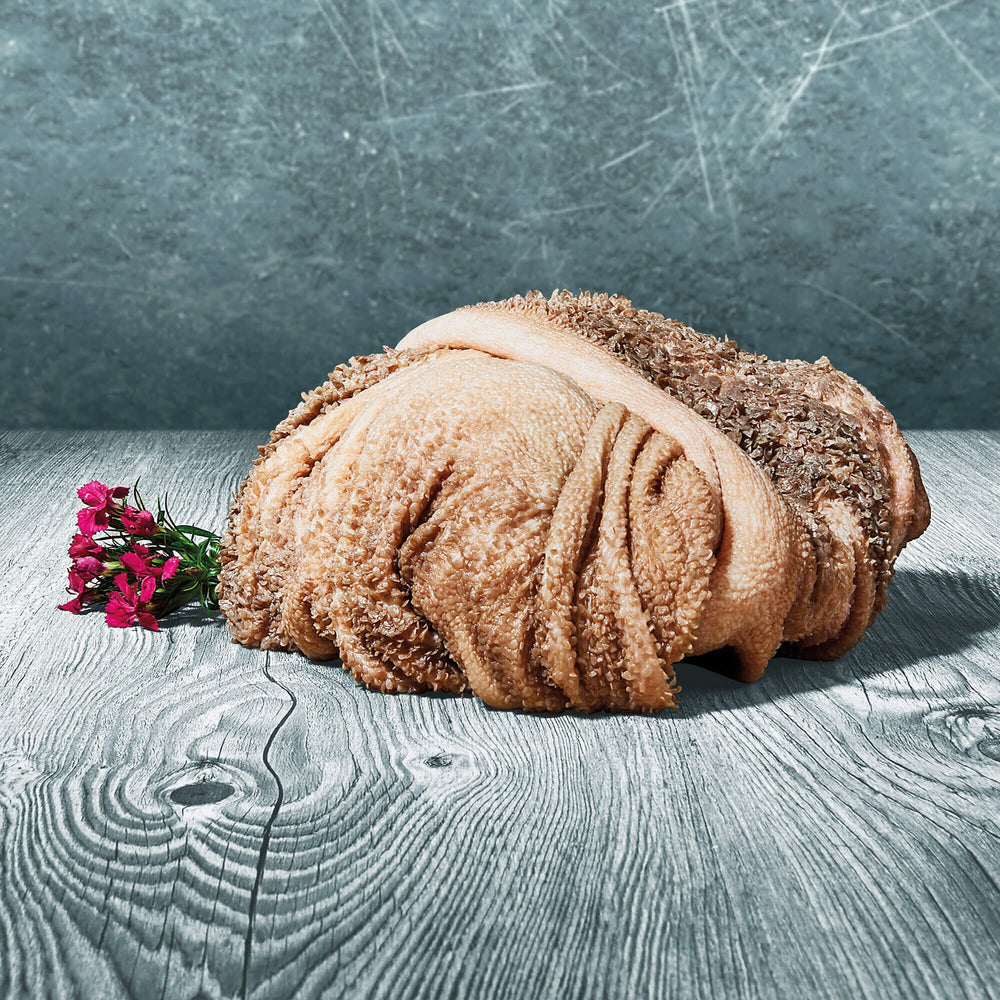 Frischer Lammpansen im Stück auf Holztisch, beige-braun mit typischer Struktur, dekoriert mit kleinen roten Blüten