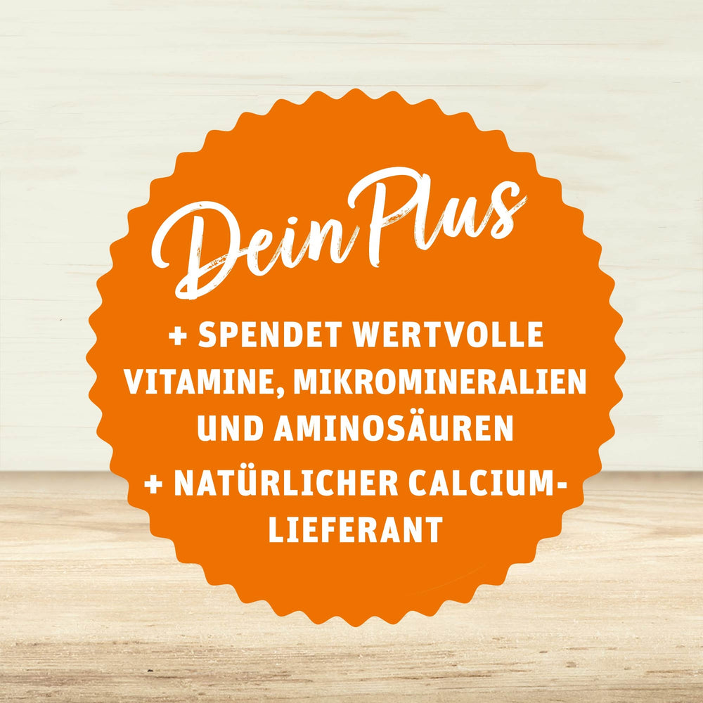 Orangefarbenes Siegel mit weißer Schrift: Dein Plus – spendet wertvolle Vitamine, Mikromineralien und Aminosäuren, natürlicher Calcium-Lieferant, auf hellem Holzuntergrund