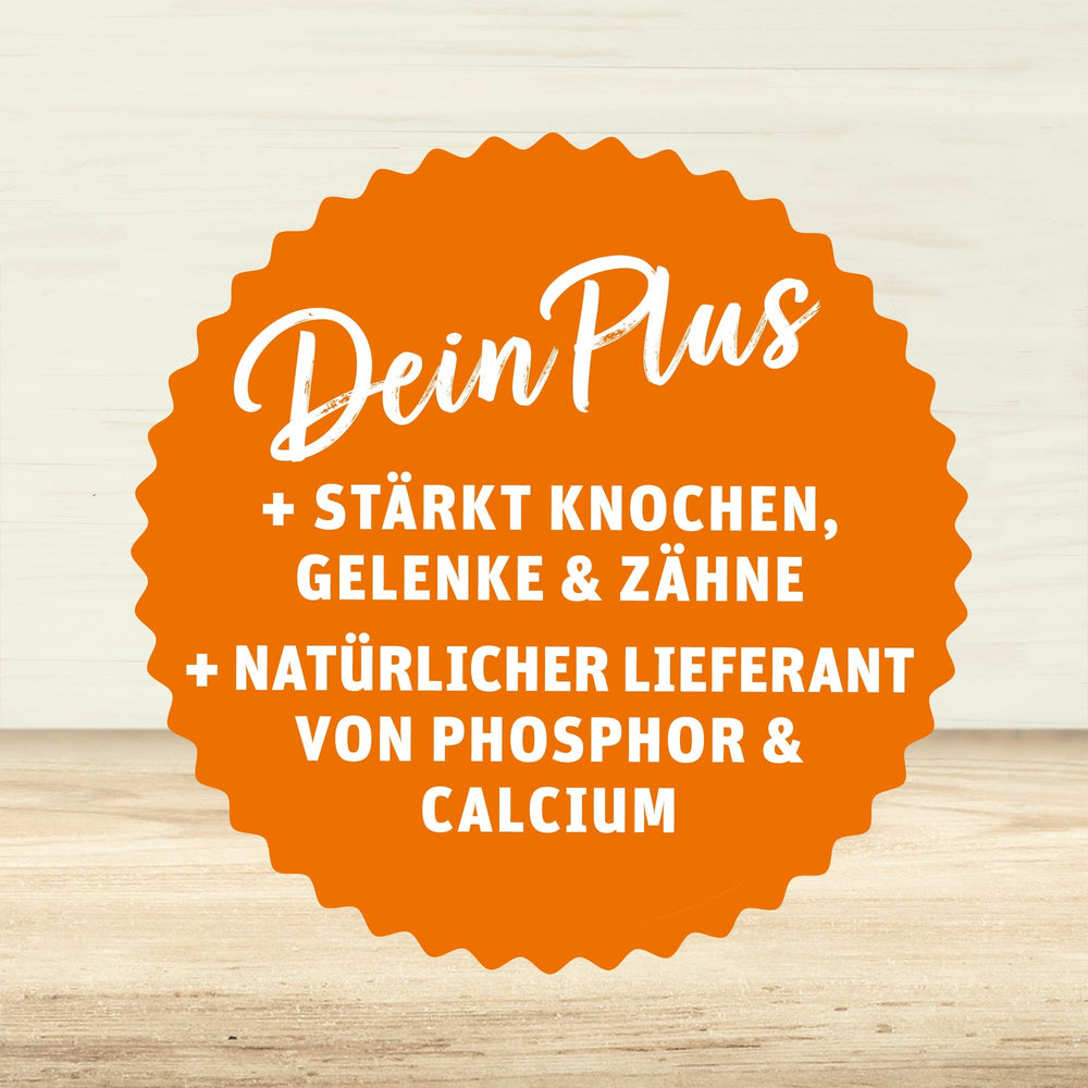 Orangefarbenes Siegel mit weißer Schrift: Dein Plus – stärkt Knochen, Gelenke & Zähne, natürlicher Lieferant von Phosphor & Calcium, auf hellem Holzuntergrund