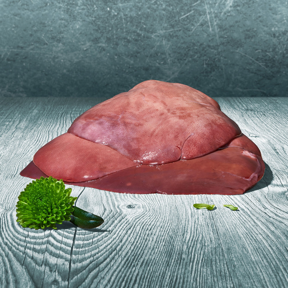 Ganze BARF-Lammleber im Stück auf einer Holzoberfläche, daneben eine grüne Blüte als Dekoration