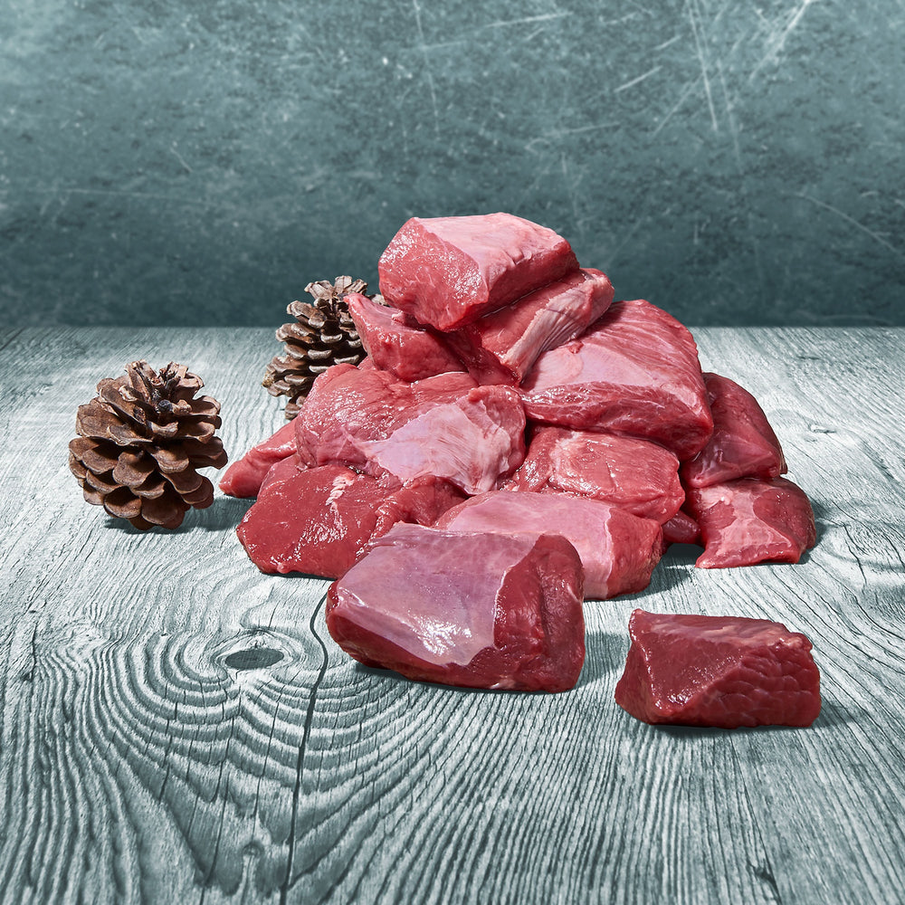 Rohes Hirschmuskelfleisch in Würfeln auf rustikalem Holzuntergrund, daneben zwei Tannenzapfen