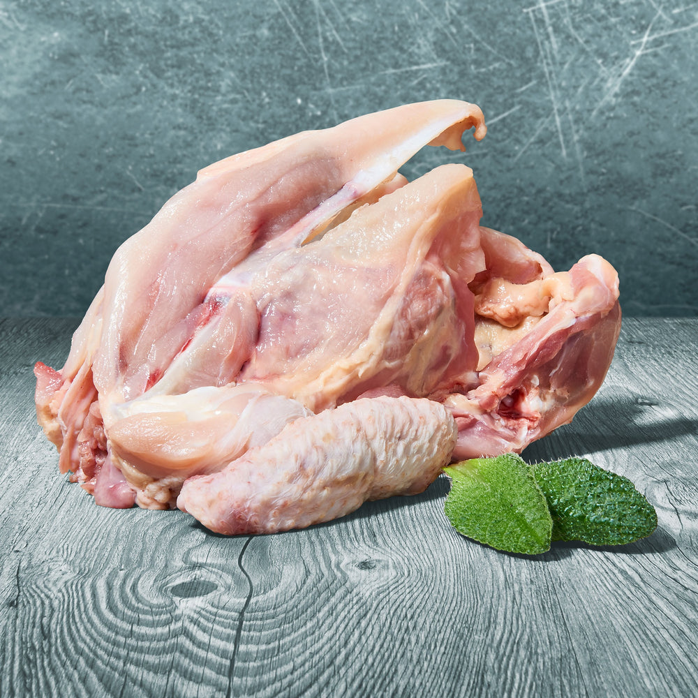 Rohes Stück einer Hühnerkarkasse auf Holztisch mit grünen Blättern dekoriert