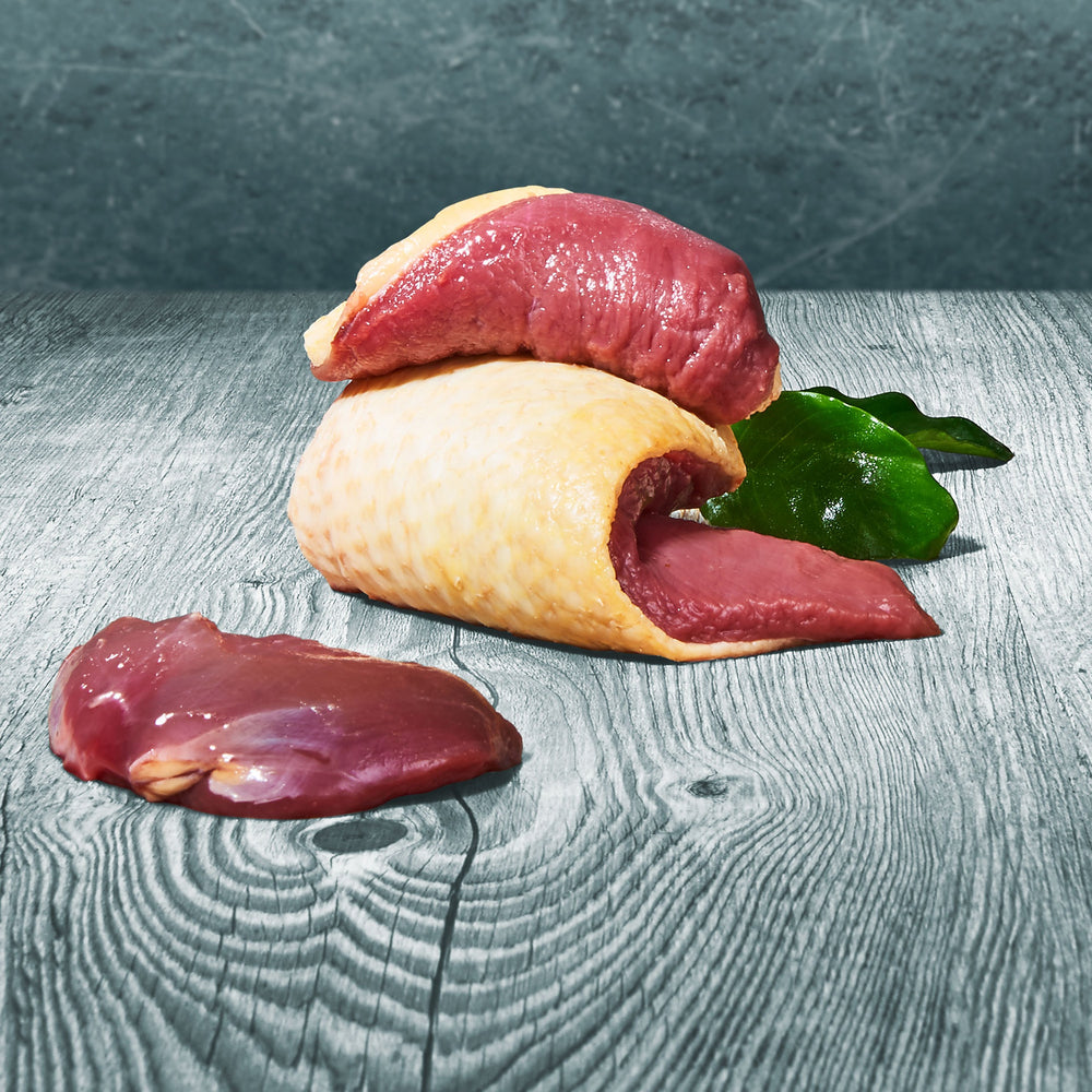 Rohe Stücke BARF-Entenmuskelfleisch mit Haut auf Holztisch, dekoriert mit grünen Blättern