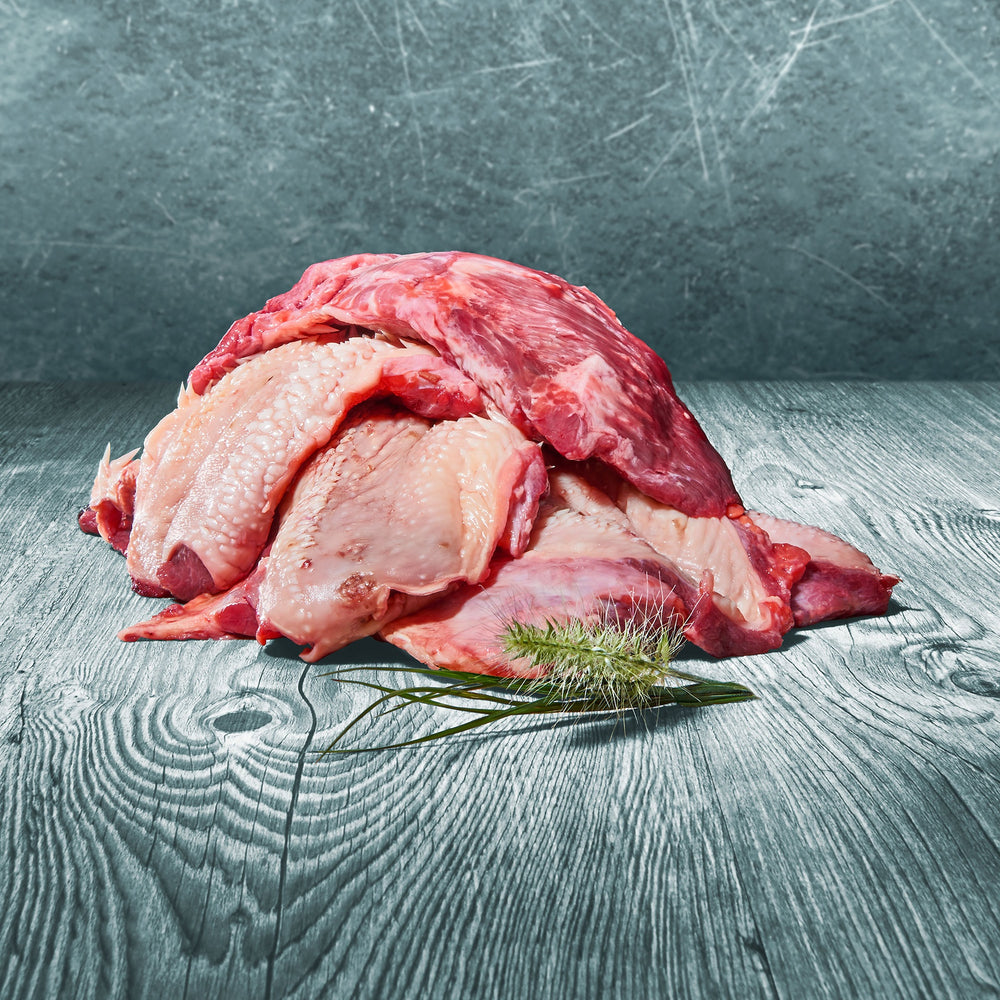 Rohe Stücke BARF-Rinderkopffleisch auf Holztisch mit grünem Ziergras dekoriert