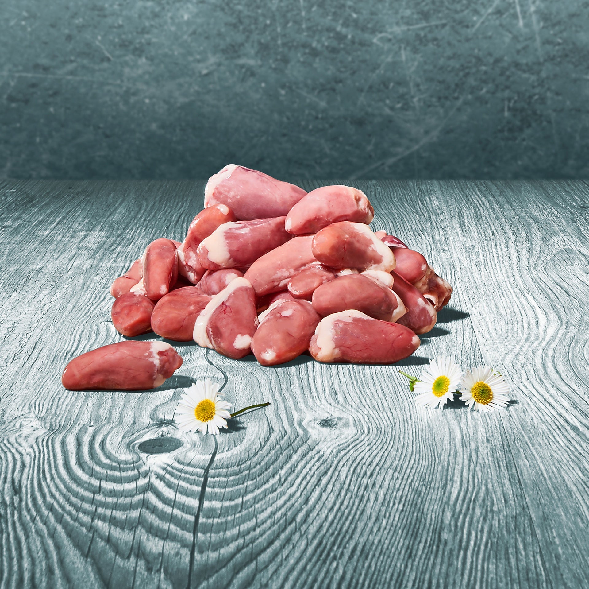 Rohe BARF-Hühnerherzen liegen auf einem Tisch neben Gänseblümchen-Dekoration