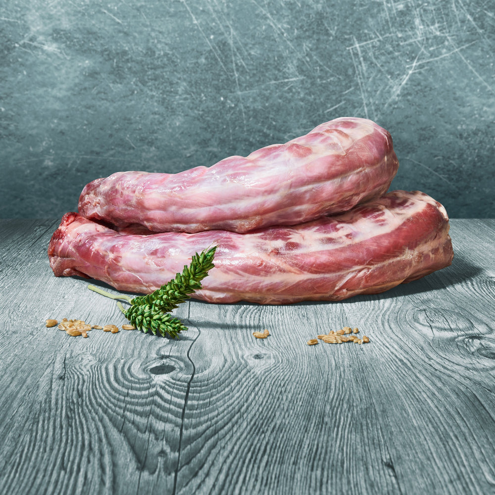 Zwei rohe Putenhälse auf Holztisch mit grünem Getreideährenzweig dekoriert