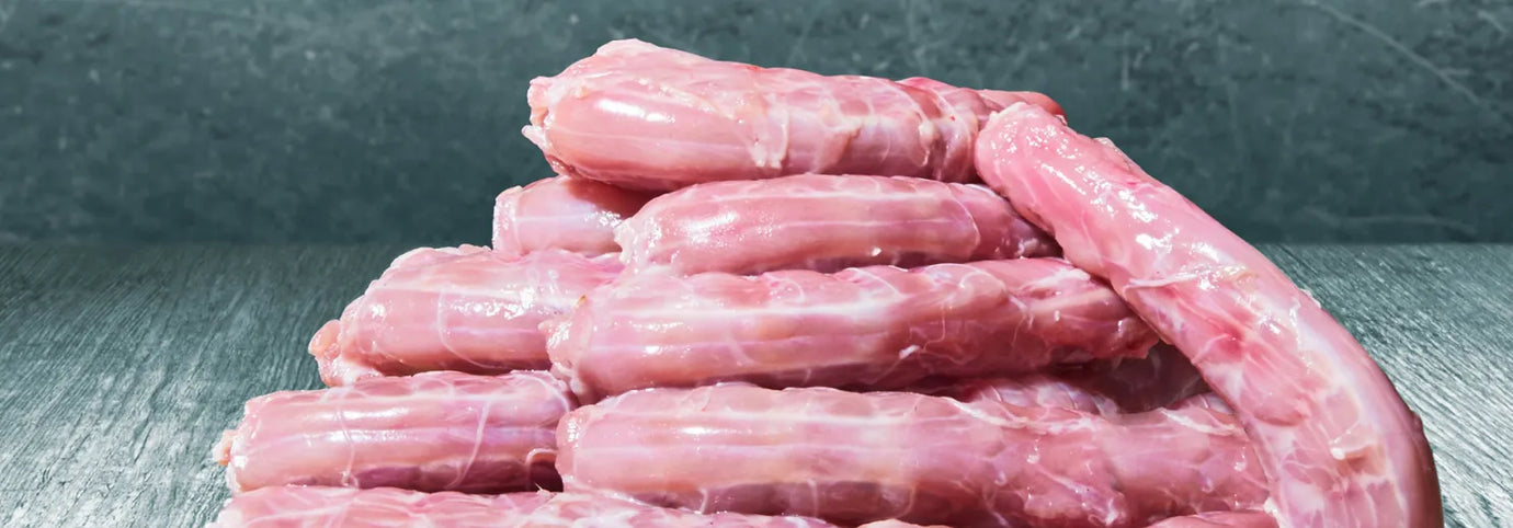 Ein Stapel roher, frischer Hälse vom Geflügel liegt auf einer grauen Oberfläche – naturbelassene Barfknochen für Hunde und Katzen