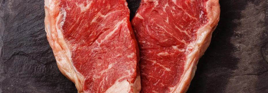 Zwei Stücke rohes Rindfleisch auf dunkler Oberfläche – Beispielbild für den Unterschied zwischen Sehnen und Fett beim Barfen