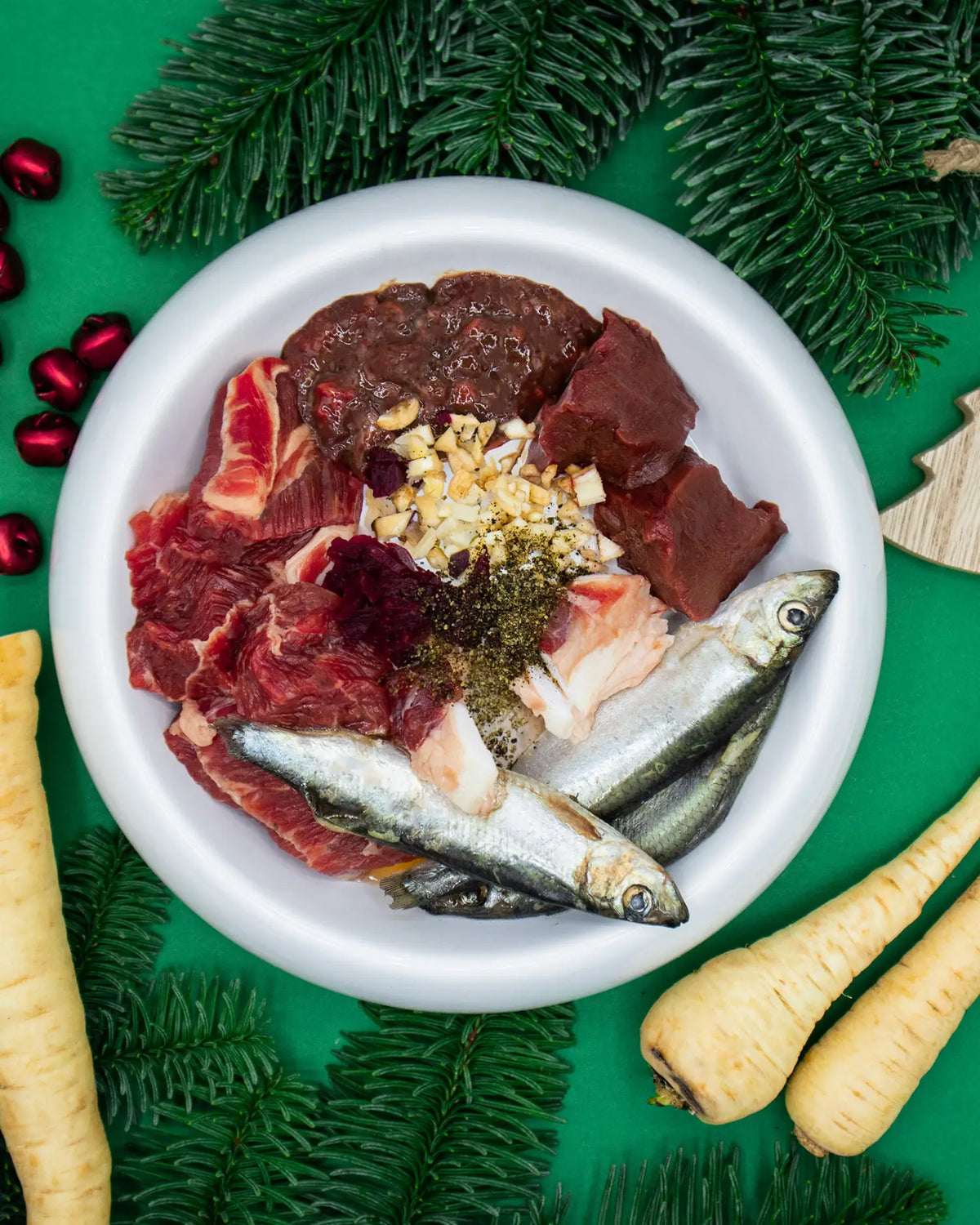 BARF-Napf mit Muskelfleisch, Innereien, ganzen Sardinen, Knochenstücken, geriebener Roter Bete und grünem Gemüse, dekoriert mit Tannenzweigen und Pastinaken