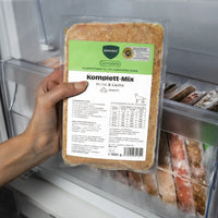 Eine Hand hält eine 500g-Packung BARFER’S Komplett-Mix Huhn & Lachs für Hunde im Gefrierfach, mit grünem complete-Label und sichtbarem DLG-Qualitätssiegel