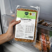 Eine Hand hält eine 500g-Packung BARFER’S Komplett-Mix Kaninchen & Lamm für Hunde im Gefrierfach, mit grünem Label, DLG-Zertifizierung und gewolftem Fertigbarf