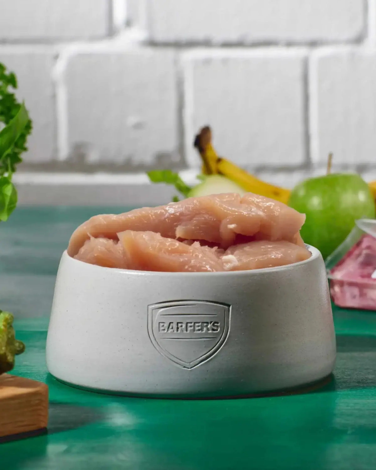 Purinbewusster BARF-Napf für Dalmatiner mit rohem Hühnerbrustfilet ohne Haut als Muskelfleisch-Basis im BARFER'S Napf, im Hintergrund Apfel, Banane und frisches Grün als pflanzlicher Anteil