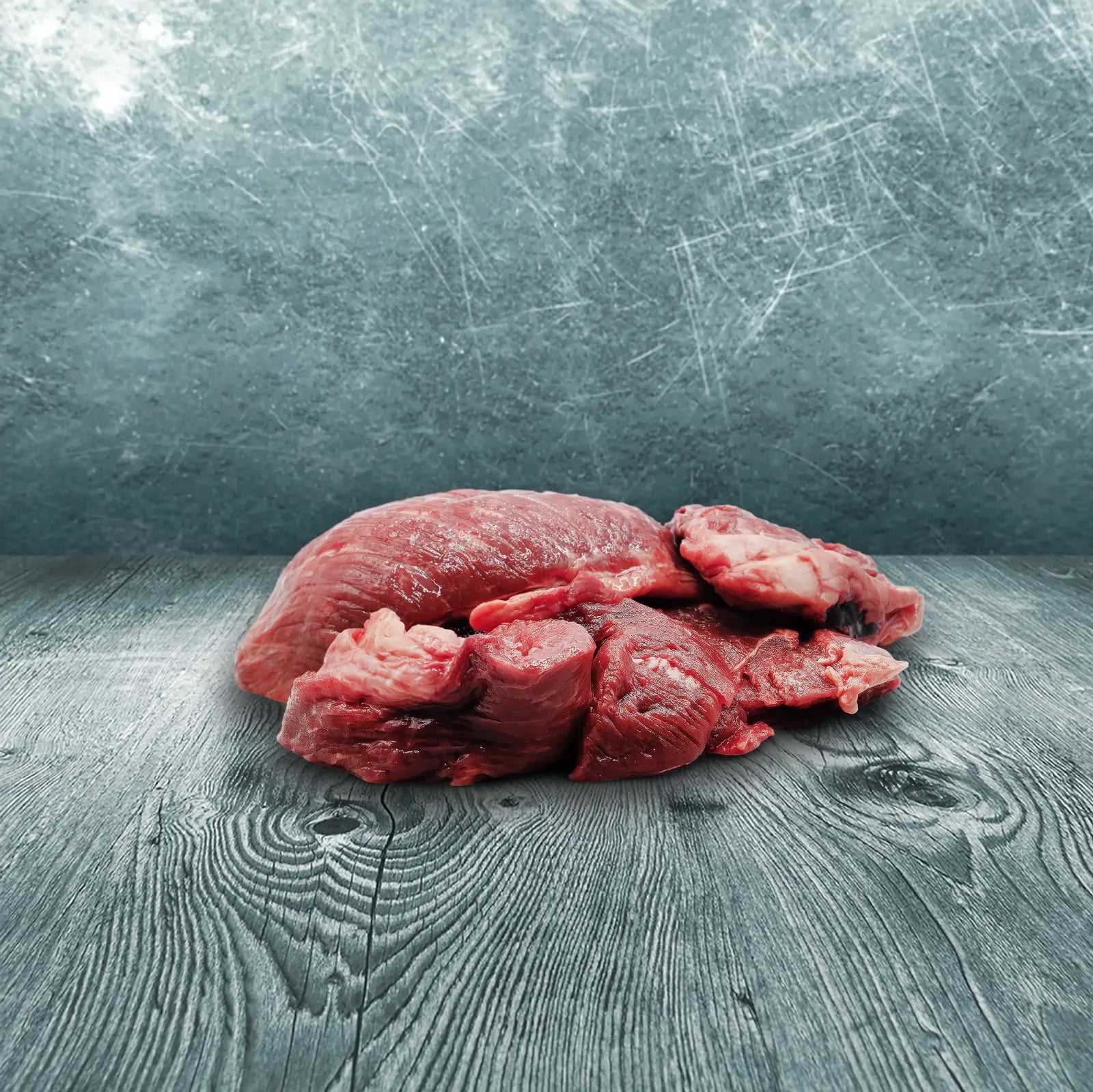 Stückiges Rinderstichfleisch als rohes Muskelfleisch für Hunde und Katzen zur BARF-Ernährung auf Holzuntergrund