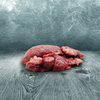 Stückiges Rinderstichfleisch als rohes Muskelfleisch für Hunde und Katzen zur BARF-Ernährung auf Holzuntergrund