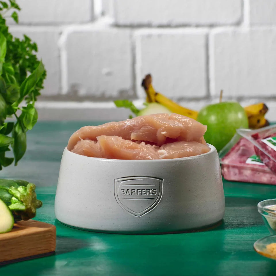 Hähncheninnenfilet im Ganzen im grauen BARFER’S Napf – frisches BARF-Muskelfleisch für Hunde und Katzen mit Zutaten im Hintergrund