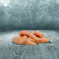 Rohes BARFER’S Hähncheninnenfilet im Ganzen als mageres Muskelfleisch für Hunde und Katzen auf grauer Holzoberfläche