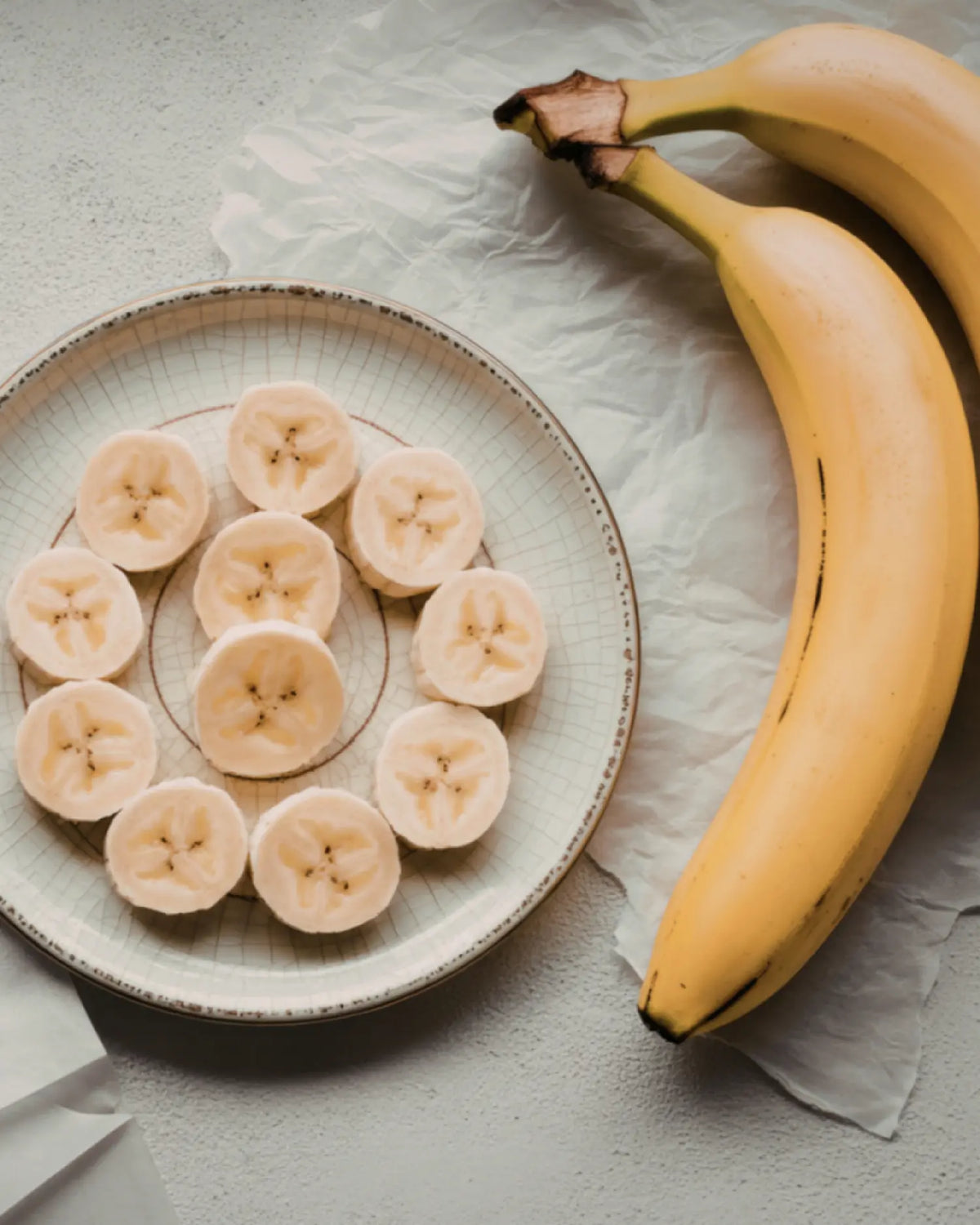 In Scheiben geschnittene Banane auf einem Teller neben zwei ganzen Bananen