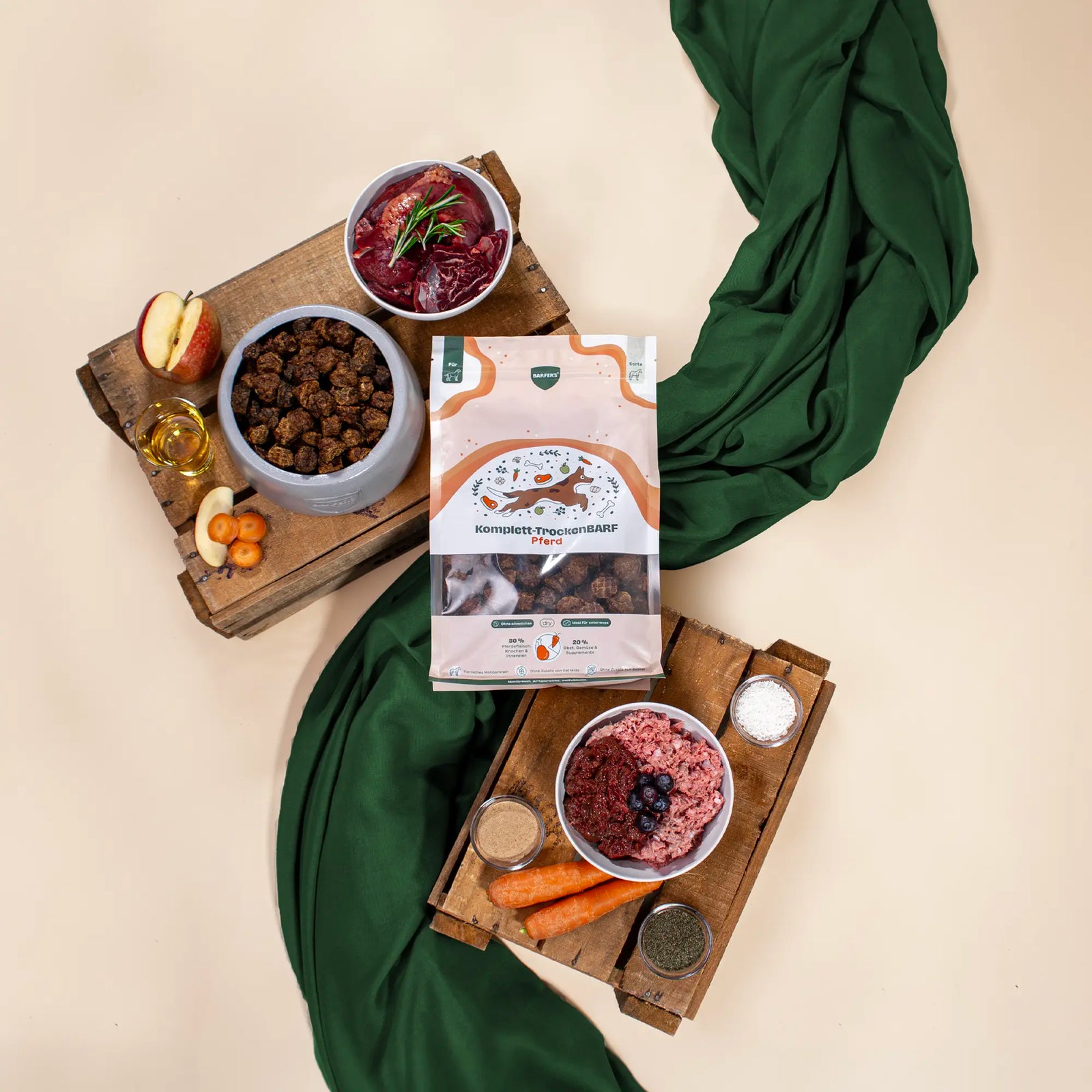 BARFER’S Komplett-TrockenBARF Pferd Verpackung umgeben von frischen BARF-Zutaten wie rohem Pferdefleisch, Knochen, Innereien, Karotten, Apfel, Beeren, Öl und Kräutern auf Holzbrettern vor hellem Hintergrund mit grünem Tuch