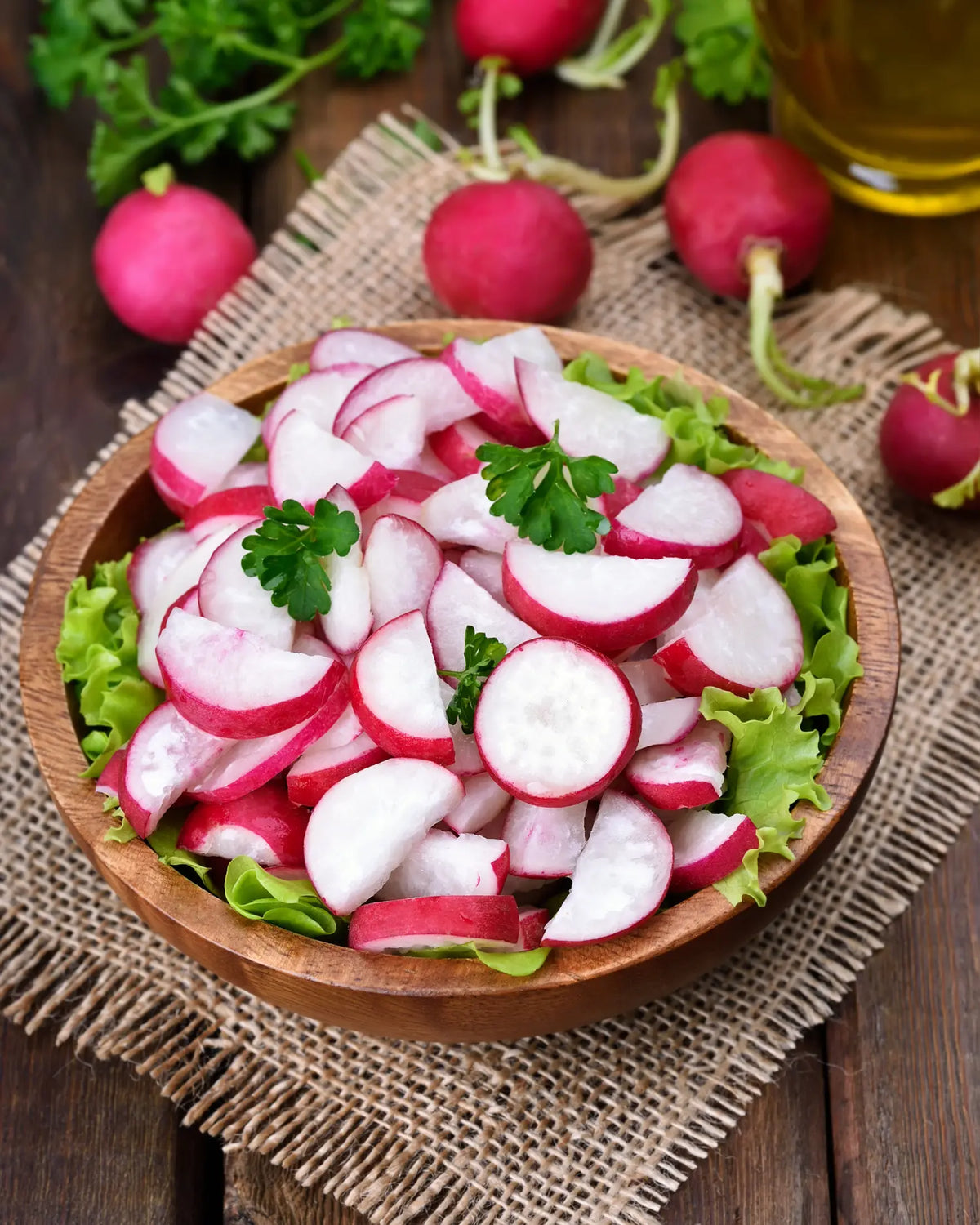 In Scheiben geschnittene Radieschen auf Salatblättern in einer Holzschale, daneben frische, ganze Radieschen