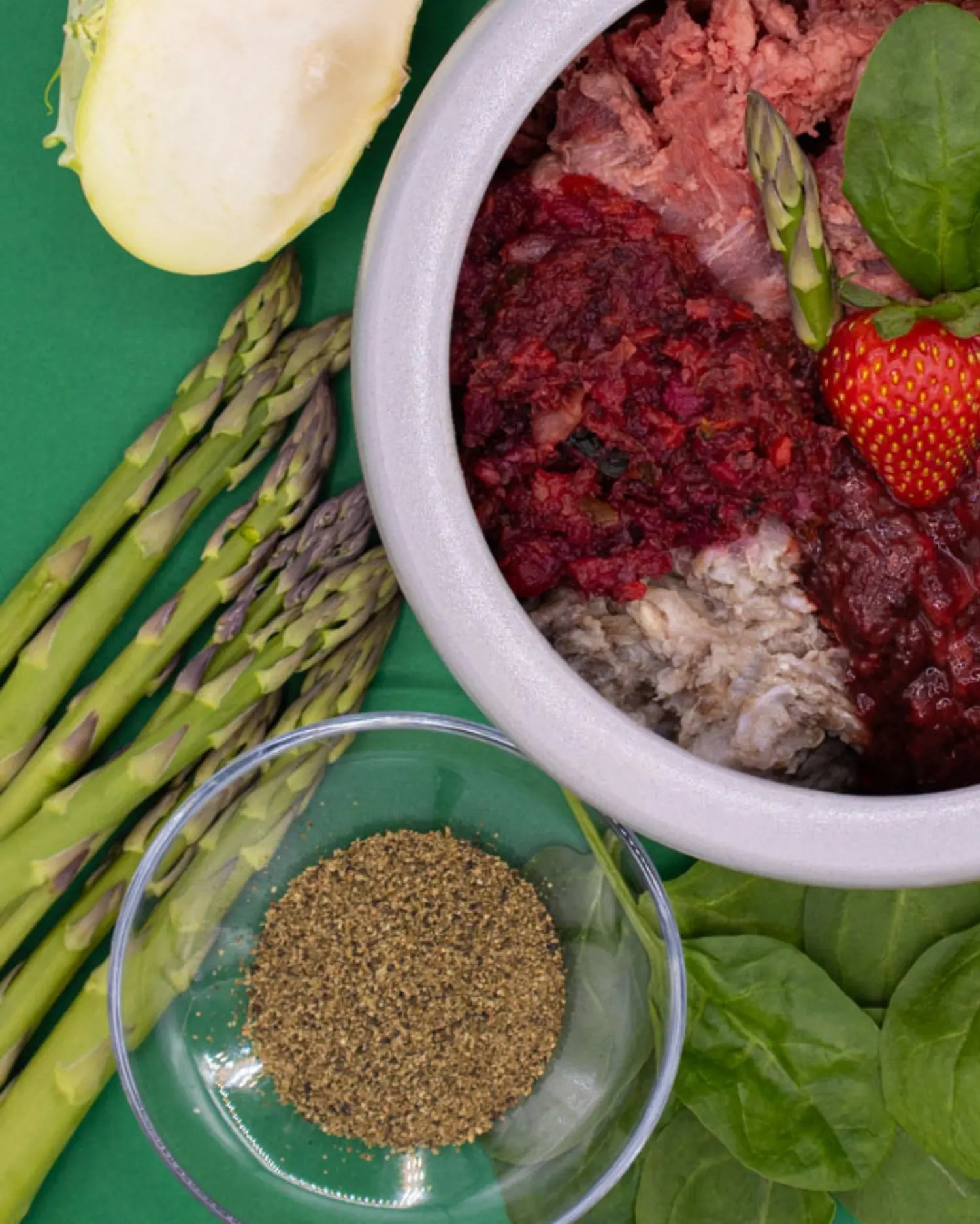 BARF-Napf für Hunde mit rohem Fleisch, püriertem Gemüse und Beeren, daneben frischer grüner Spargel, Zucchini und gemahlene Kräuter – Beispiel für Spargel als ergänzende Zutat in der Hundeernährung
