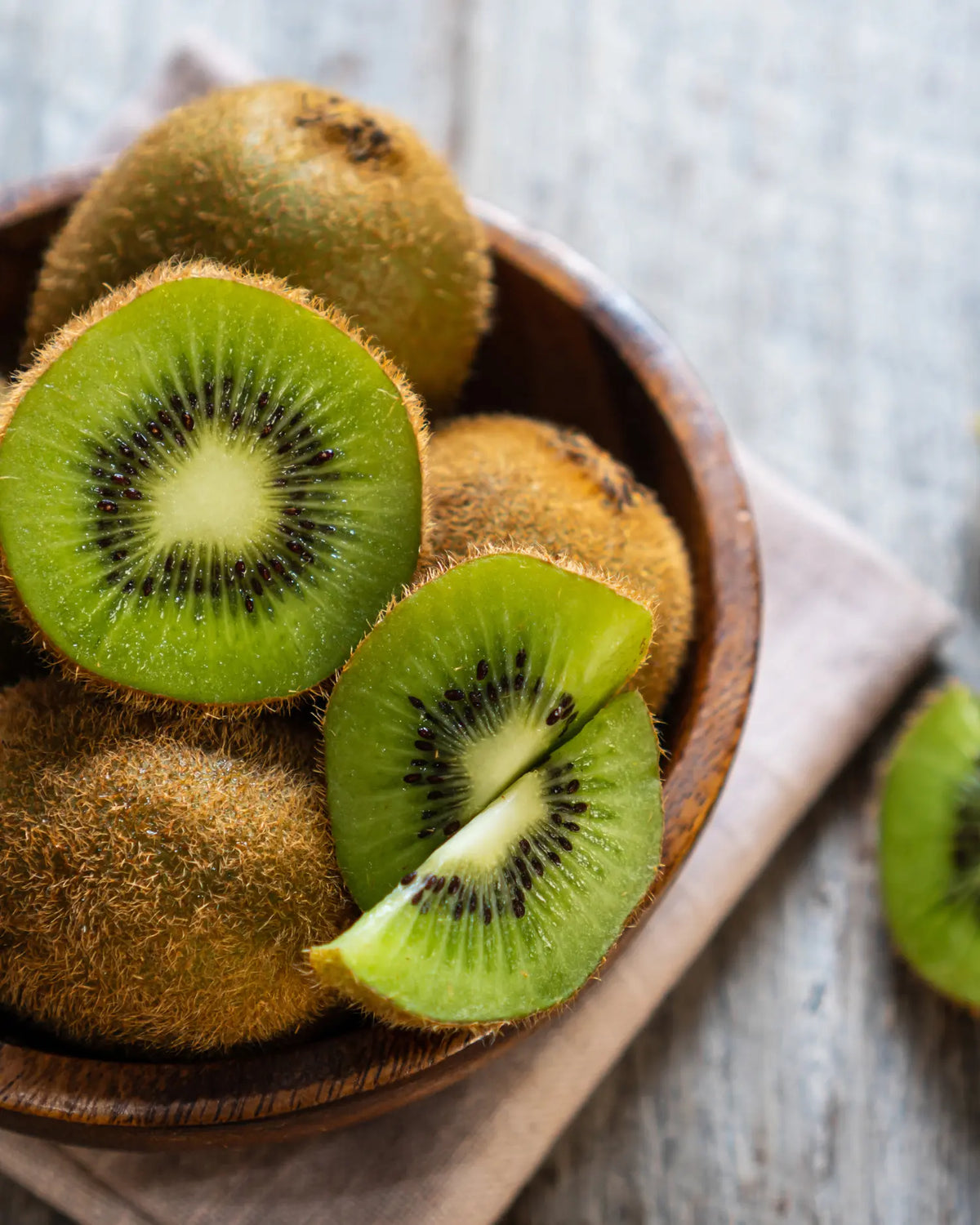 Kiwis in einer Holzschale, teils halbiert und in Spalten geschnitten, mit sichtbarem Fruchtfleisch und Kernen
