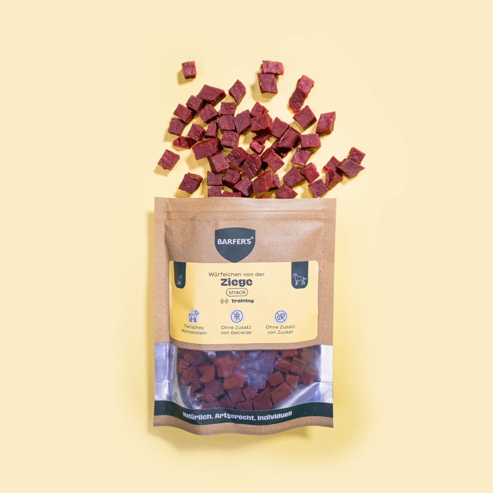 Gewürfelte und luftgetrocknete Leckerli von der Ziege liegen oberhalb einer geöffneten Verpackung "Würfelchen von der Ziege" der Marke BARFER’S