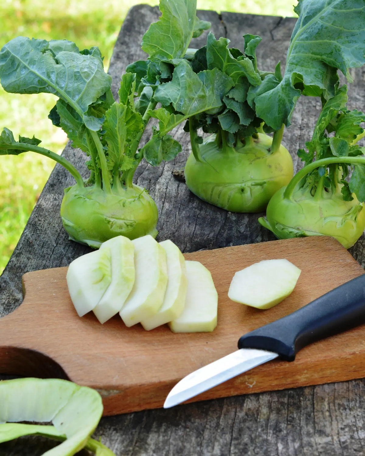 Ganze Kohlrabi mit Blättern und geschälte, in Scheiben geschnittene Kohlrabi auf einem Holzbrett mit Messer