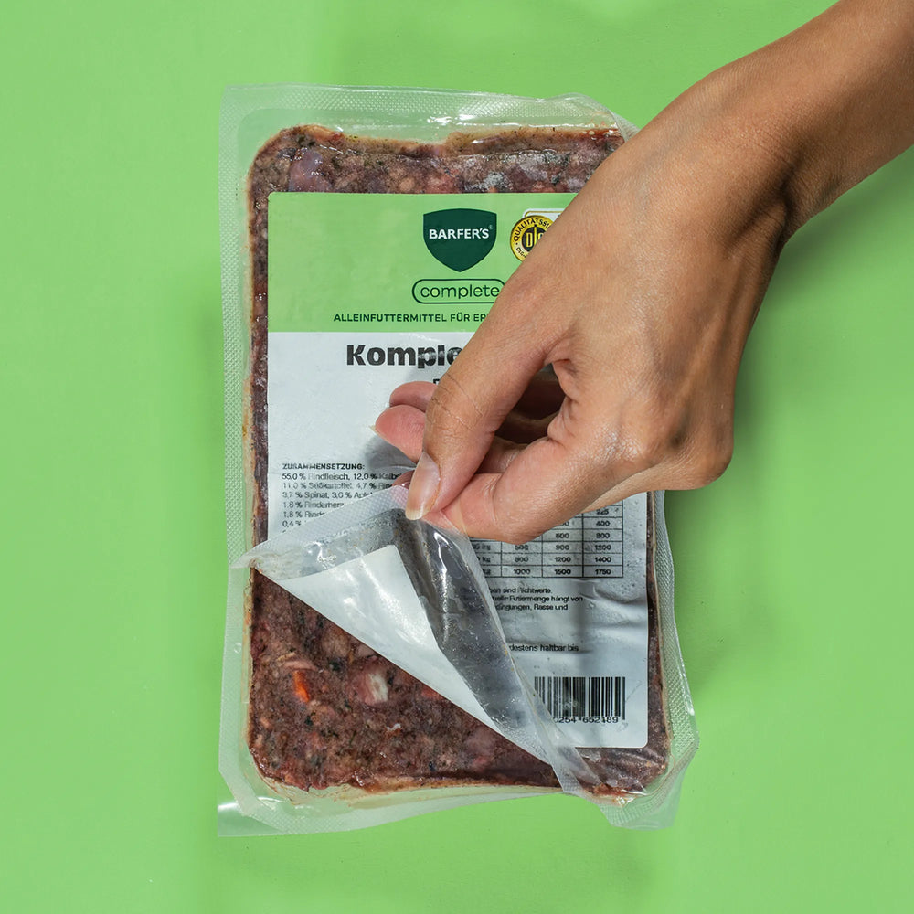Hand öffnet eine 500-g-Vakuumpackung BARFERS Complete Komplett-Mix, Fertigbarf für Hunde