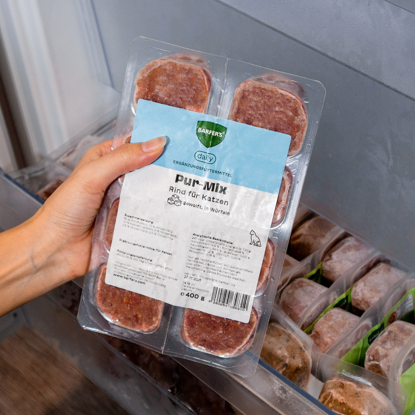Eine Hand hält eine 400g Verpackung vom BARFER’S Pur-Mix Rind für Katzen – gewolftes Rindfleisch mit Herz, Kalbsbrustbein, Leber, Niere und Milz in praktischer Würfelform