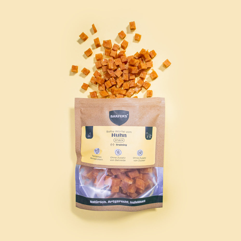 Gewürfelte und luftgetrocknete Leckerli vom Huhn liegen oberhalb einer geöffneten Verpackung "Softe Würfel vom Huhn" der Marke BARFER’S.